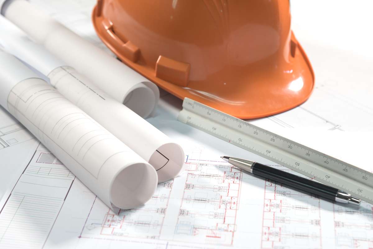 Blueprints, a hard hat, and a pen on the table.