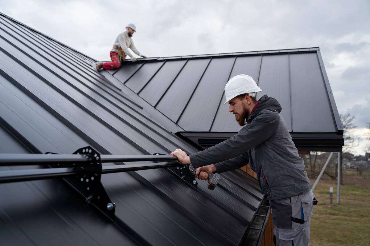 Workers installing safety rails on a black metal roof.