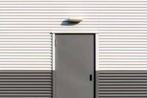 a grey metal door on a corrugated metal wall with a light above it